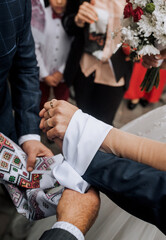 Parents of newlyweds help tie a knot from an embroidered towel on the hands of the bride and groom at the ceremony. Wedding photography, Ukrainian tradition, ritual.