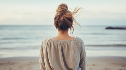 Woman meditating at the beach, near the ocean, back view, the wind blows the hair - obrazy, fototapety, plakaty