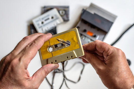 Rebobinando manualmente una cinta de casete con la ayuda de un boli, reproductor de casetes y varias cintas sobre fondo blanco.