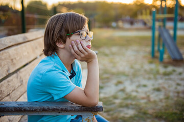 Upset kid problem sitting on play park playground bench. Concept bullying, depression, child...