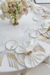 Impeccable setting of wedding table with classic dishes, silverware, white table textiles, crystal.
