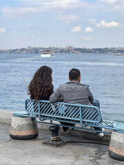 couple sitting on bench by sea under beautiful sky