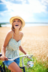 Woman laughing on bicycle in the countryside, happiness and travel on journey or thinking outdoor. Funny, bike and excited person smile at field on transport, freedom and cycling in nature in summer