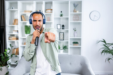 Carefree man dancing while listening to music at home singing karaoke ponting finger at camera