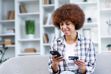 smiling millennial woman holding smartphone and banking credit card, involved in online mobile shopping at home, happy female shopper purchasing goods or services in internet store.