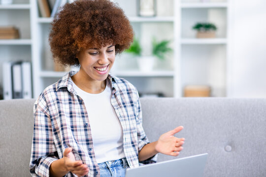 Relaxed happy young woman sitting on sofa using laptop at home surfing, doing online ecommerce shopping, looking at computer ordering sale products on website, video conference