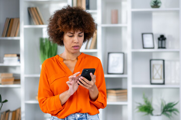 Young business woman wearing casual clothes standing at modern office using applications on cell phone, reading news on smartphone, fast connection, checking mobile apps indoors.