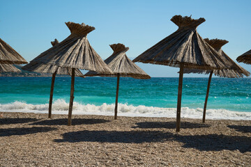 A beautiful beach with small golden pebbles and straw umbrellas on the turquoise seashore.