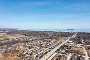 Aerial view of Barrie, Ontario, highlighting dense residential areas adjacent to the expansive, icy expanse of Lake Simcoe. The urban landscape showcases modern homes and infrastructure against a sere