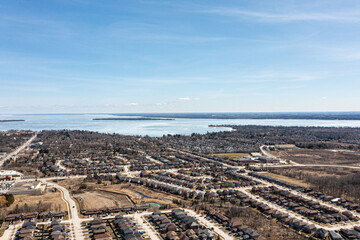 Obraz premium Aerial view of Barrie, Ontario, highlighting dense residential areas adjacent to the expansive, icy expanse of Lake Simcoe. The urban landscape showcases modern homes and infrastructure against a sere
