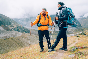 Caucasian and Sherpa men with backpacks with trekking poles together smiling enjoying Mera peak climbing acclimatization walk  Makalu Barun Park route. Backpackers enjoying beautiful valley view - obrazy, fototapety, plakaty