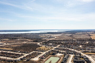 Aerial view of Barrie, Ontario, highlighting dense residential areas adjacent to the expansive, icy expanse of Lake Simcoe. The urban landscape showcases modern homes and infrastructure against a sere