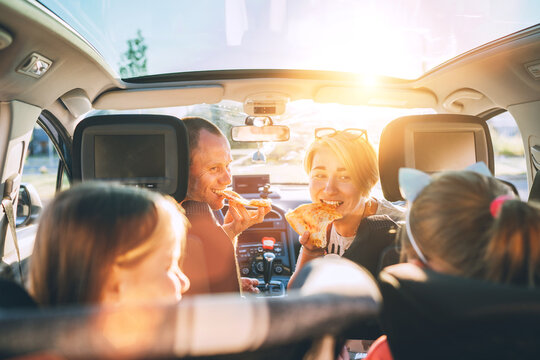Portrait of young woman eating just cooked Italian pizza while she traveling with family in modern car. Happy family moments and values, fast food eating or auto journey lunch break concept image.