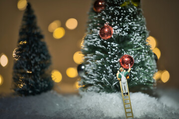 A painter on a ladder paints the colorful balls on a huge Christmas tree, miniature figure scene,...