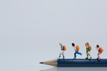 Schoolchildren with schoolbags walk on a sharp pencil, miniature figures scene, white background,...