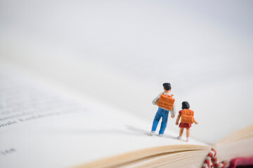 Schoolchildren with schoolbags walk on an open book, miniature figures scene - obrazy, fototapety, plakaty