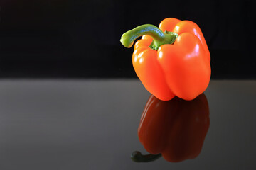 Orange bell pepper isolated on a black reflective surface.