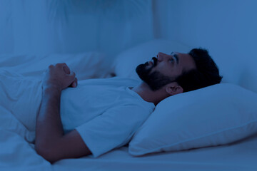 Awake sleepless upset indian man lying in bed alone at night