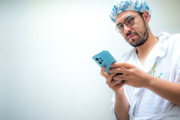 Man wearing towel and bathing cap looking blue smartphone