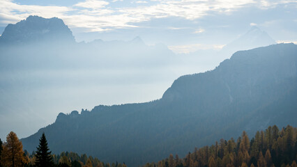 Autumn alpine landscape with big hazy mountains and some golden larches in foreground, Italy, Europe