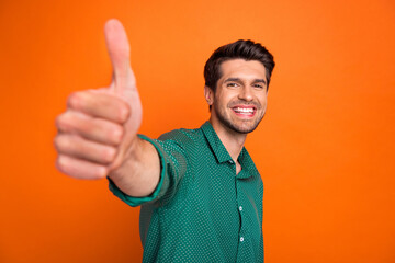 Photo of cheerful funky guy wear green shirt showing you thumb up isolated orange color background