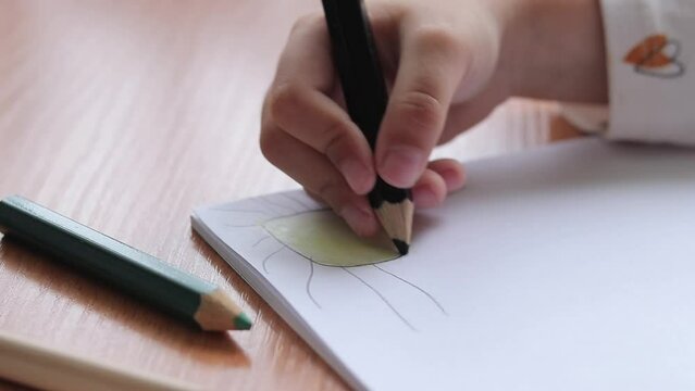 A child draws with colored pencils in an album. Children's creativity, learning in kindergarten, school or at home. Child's hand with a pencil close-up, selective focus. Girl draws a picture