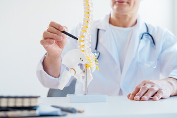 Closeup no face medical male doctor pointing on human spine model with a pen sitting in his office....