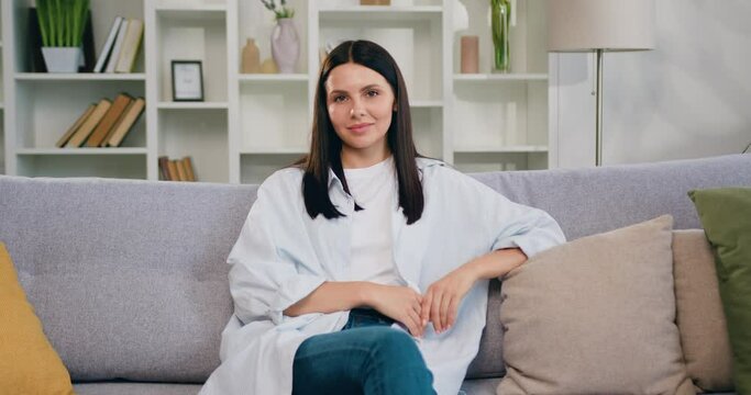 Close-up. Portrait petty house wife relax on comfort sofa smile staring at camera look happy. Happy woman sitting on sofa at home and looking at camera.