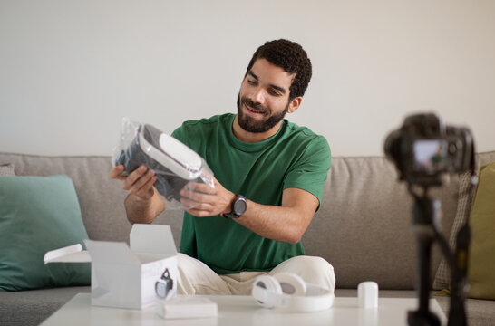 Happy young arab guy blogger gamer shows vr glasses, shooting video on camera