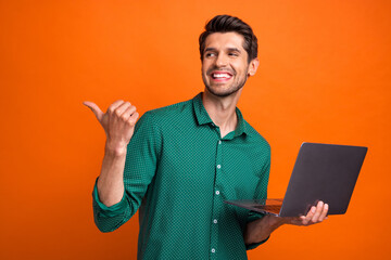 Photo of cheerful dreamy man dressed green shirt typing modern device thumb empty space isolated orange color background