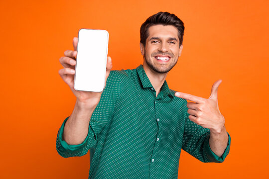 Photo of young man student wear green shirt point finger smartphone gadget modern app display web store isolated on orange color background