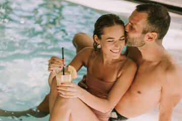 Young couple relaxing by the indoor swimming pool - obrazy, fototapety, plakaty