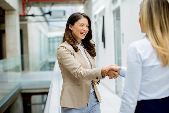 Two young business women handshaking  in the office hallway