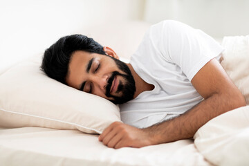 Smiling Young Indian Man Sleeping Calmly In Comfortable Bed At Home