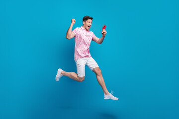 Full length profile portrait of delighted crazy person jump run raise fist use smart phone isolated on blue color background