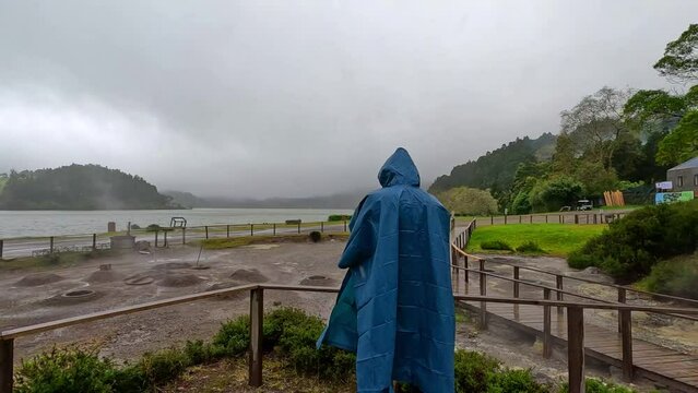 A man with a blue raincoat taking pictures of the geysers where the stew (Cozinhou) is cooked in the ground in the hot water in Furnas, Azores, Portugal