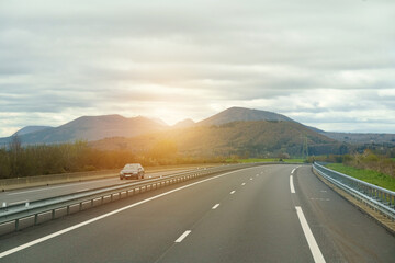 A lonely car drives along a motorway in France in the rays of the setting sun against the backdrop...