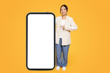 Happy chinese millennial lady in suit, point finger at big smartphone with empty screen