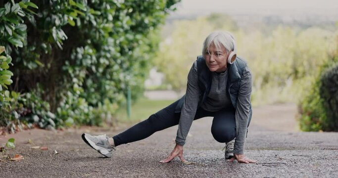Fitness, senior woman and stretching body in a road with music headphones for training in nature. Legs, stretch and elderly lady with ground exercise in park for morning cardio with podcast or radio