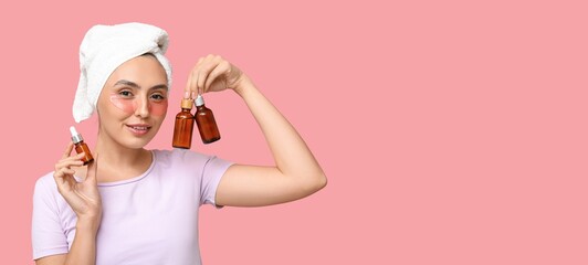 Beautiful young woman with under-eye patches holding bottles of cosmetic oil on pink background...