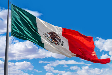 Flag of Mexico on a pole with a background of blue cloudy sky