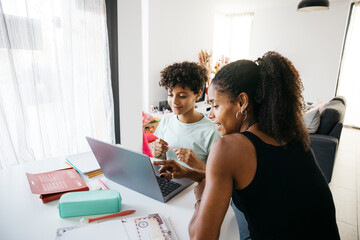 Cheerful woman helping her smiling daughter doing homework. Happy mother assisting her daughter with school homework in living room.