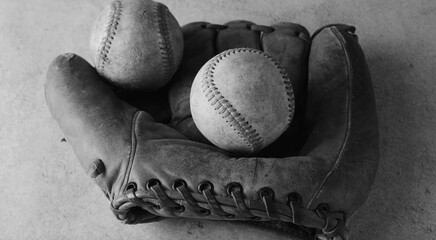 Old used baseballs in vintage leather ball glove for sports nostalgia background in black and white.