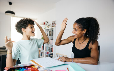 Cheerful woman helping daughter doing homework. Mother and daughter shaking hands while doing...
