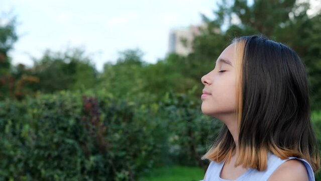 Portrait of a young beautiful preschool girl enjoying a warm summer day outdoors. Cute girl relaxing outdoors on the street, breathing fresh air. Profile of a child's face against the backdrop of a - Powered by Adobe