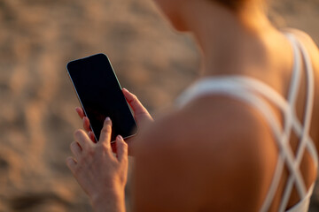 Woman at seaside, post-training, using cellphone with lank screen, mockup