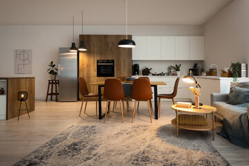 Obrazy na Plexi  Interior of modern open plan kitchen with dining table and glowing lamps