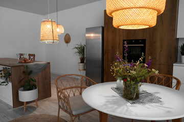 Interior of modern kitchen with glowing lamps and flower vase on dining table
