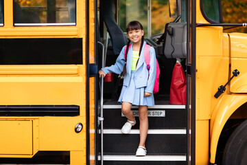 Smiling preteen asian girl getting of the yellow school bus