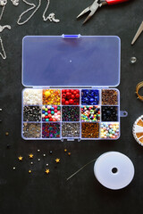 Box with colorful beads, string, wire, chain, scissors, pliers and hammer on dark background. Various jewelry making supplies. Top view.